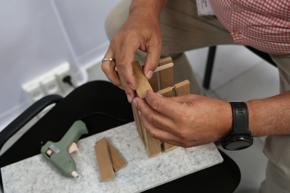 A person is trying to assemble something using a glue gun and pieces of wood.